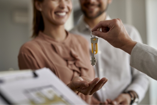 Nahaufnahme eines Immobilienmaklers, der einem Paar neue Hausschlüssel gibt